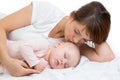 Woman and newborn boy relax in a white bedroom. Young mother kissing her newborn child. Mom nursing baby.