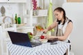 Woman with notebook and phone cooks in kitchen. Isolation period, quarantine, social distancing. Remote education or remote work Royalty Free Stock Photo