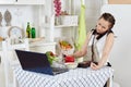 Woman with notebook and phone cooks in kitchen. Isolation period, quarantine, social distancing. Remote education or remote work Royalty Free Stock Photo