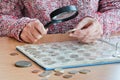 Woman-numismatist views coins from a coin album through a magnifying glass