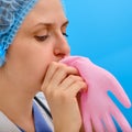 Woman nurse blows up a pink medical glove, close-up on a blue background. Doctor puff a protective glove with air, concept