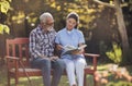 Woman nurse reading book to senior man in park Royalty Free Stock Photo