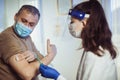 Woman nurse with surgical mask and face shild giving injection to senior man. Covid-19 or coronavirus vaccine Royalty Free Stock Photo