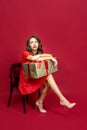 Woman offended and sits on a chair with a gift on a red background