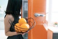 Woman open refrigerator door in the kitchen. Orange in hand