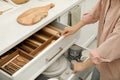 Woman opening drawers of kitchen cabinet with different dishware and utensils, closeup Royalty Free Stock Photo
