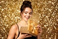 Woman opening Gift Box. Happy Girl holding Golden Present over Gold Glitter background. Beauty Model get Surprise on Christmas Royalty Free Stock Photo