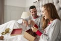 Woman Opening Gift Of Necklace In Bed At Home As Couple Exchange Presents On Christmas Day Royalty Free Stock Photo