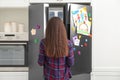 Woman opening refrigerator door with drawings, notes and magnets in kitchen Royalty Free Stock Photo