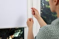 Woman opening white roller blind on window, closeup
