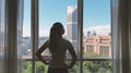 Woman opens curtain on the big windows city view with green gadern and buildings. Green city concept.