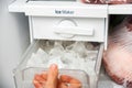 A woman opens an ice maker tray in the freezer to take ice cubes to cool drinks