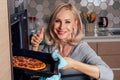 Woman openung ovens and take pizza with tomatoes, olives, mushrooms and cheese sausage