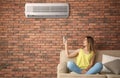 Woman operating air conditioner while sitting on sofa at home Royalty Free Stock Photo