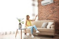 Woman operating air conditioner while sitting on sofa Royalty Free Stock Photo