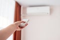 Woman operating remote controller on air conditioner inside the room, copy space. Hand with remote control directed on conditioner Royalty Free Stock Photo