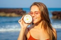 Woman in orange coral bikini and cool pink glasses standing on the beach with fresh dry open coconuts in hand. female Royalty Free Stock Photo