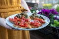 A woman in an orange dress holding a plate of home-made bruchetta with tomato and mushrooms, summer food with flowers in the