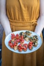A woman in an orange dress holding a plate of home-made bruchetta with tomato and mushrooms, summer food