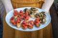 A woman in an orange dress holding a plate of home-made vegan bruchetta with tomato and mushrooms, summer food