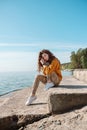 Woman in orange sweater sitting on a stone stairs on a beach with her eyes closed