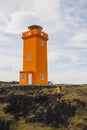 Woman in orange sweater walking near Svortuloft Lighthouse, Hellissandur Iceland