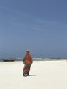 A woman in orange walks down the white beaches of Zanzibar