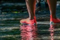 Woman in orange water shoes at a coast, shore or beach with clear water at a sunny day travels through a creek for recreation Royalty Free Stock Photo