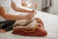 Woman organizing fall and winter warm clothing. Young woman folding sweaters on white bed. Folding laundrey