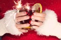Woman with red and gold nails with golden snowflakes holding cup of tea with lemon and sparkler.