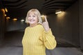 Woman over 65 in yellow sweater shows heavy metal gesture. Horns, love hard rock. Youthful spirit Royalty Free Stock Photo