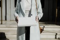 Woman in an overcoat carrying a white box in front of a building