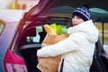 Woman with package of food opened trunk of car in parking lot of supermarket. Shopping by car Royalty Free Stock Photo