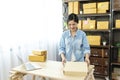 Woman packing box on table checking goods package delivery shipping to customer. Asian woman startup small business at home office