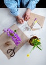 Woman packing spring potted flowers as gifts, writing postcards on white table