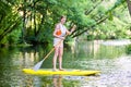 Woman paddling with surfboard sup on forest river