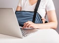 Woman with painful arm in sling using laptop for work, study. Female suffering from shoulder, clavicle ache, sitting at
