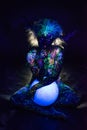 A woman painted with fluorescent powder holds a spherical lamp. Closeup of the legs of a girl`s hands with colored body