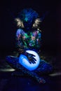 A woman painted with fluorescent powder holds a spherical lamp. Closeup of the legs of a girl`s hands with colored body