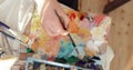 Paintress is mixing oil paints on palette using brush, hand closeup, top view.