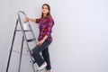 Woman painter stands on a stepladder in a plaid shirt, copy space. Painting the walls in a new apartment Royalty Free Stock Photo