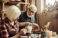 Woman painting clay pot with senior potter