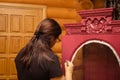 Woman painting door of wooden cupboard with carved ornaments with brush in red color. Meticulous process of patinating