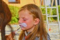 Woman painting face of kid outdoors. Baby face painting. Little girl getting her face painted like a rabbit by face painting artis Royalty Free Stock Photo