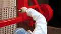 Female worker pulverizing red paint on industrial unit in workshop