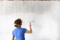 Woman painting new apartment walls in color white with paint roller. Renovating house