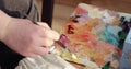 Woman paintress is mixing oil paints on palette using brush, hand closeup.