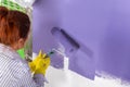 woman paints white wall and purple paint roller