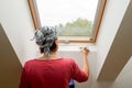 Woman paints a window recess of a roof window with a brush