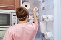 Woman in pajamas takes roll of toilet paper from fridge